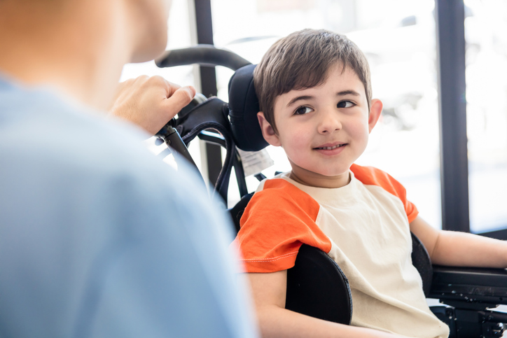 A young boy in a wheelchair smiling at an adult.