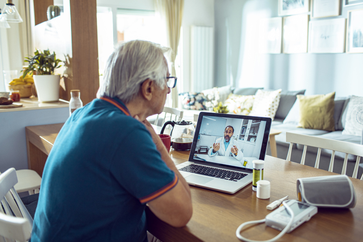 A man with grey hair is watching the laptop screen.