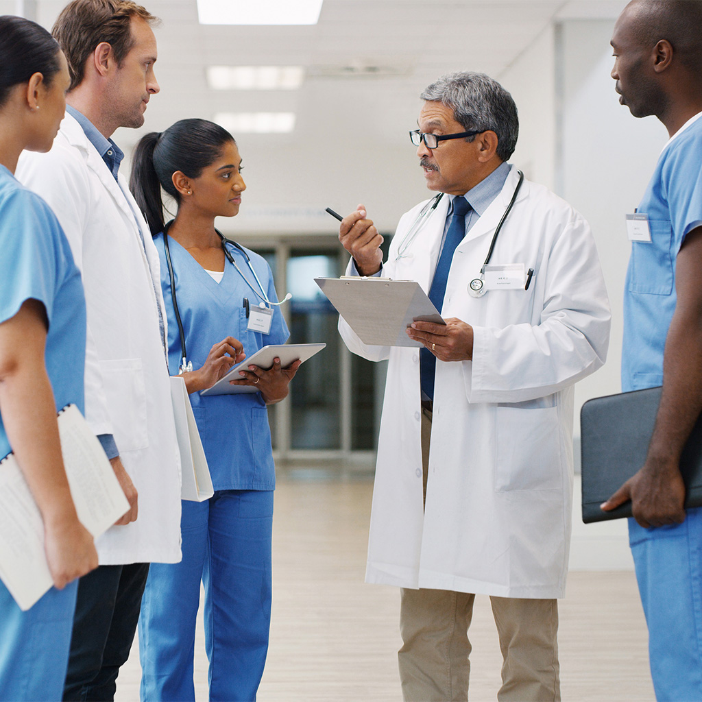 A team of doctors and nurses have a conversation in a hospital hallway