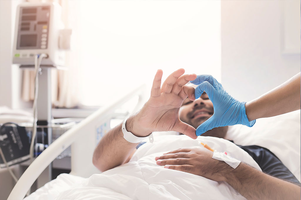 A patient in a bed makes a heart with his hands with a nurse wearing gloves