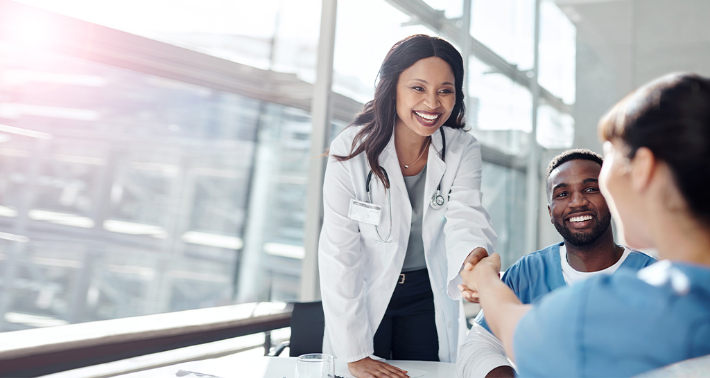 A doctor in white lab coat shakes hands with a nurse in scrubs