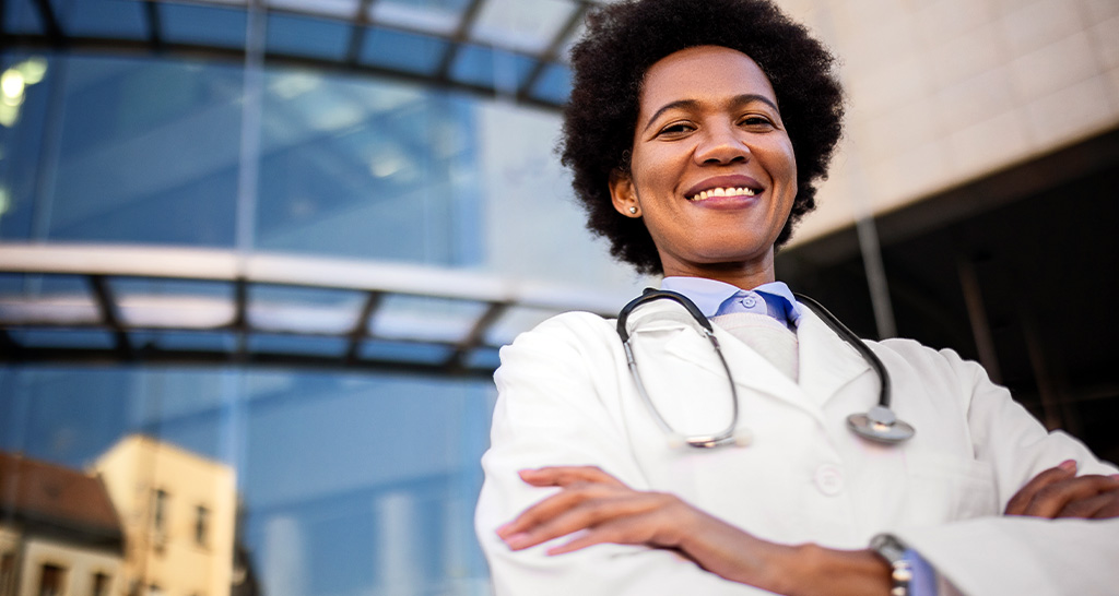 A doctor in white lab coat poses in front of her hospital