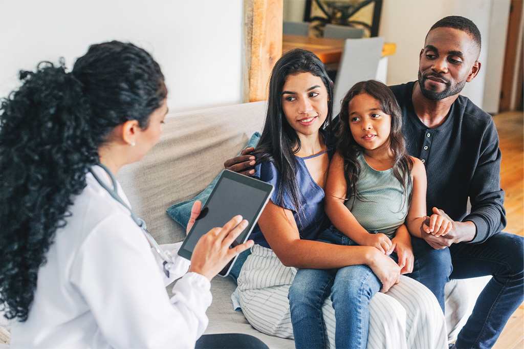 Two parents and their young daughter speak to a doctor