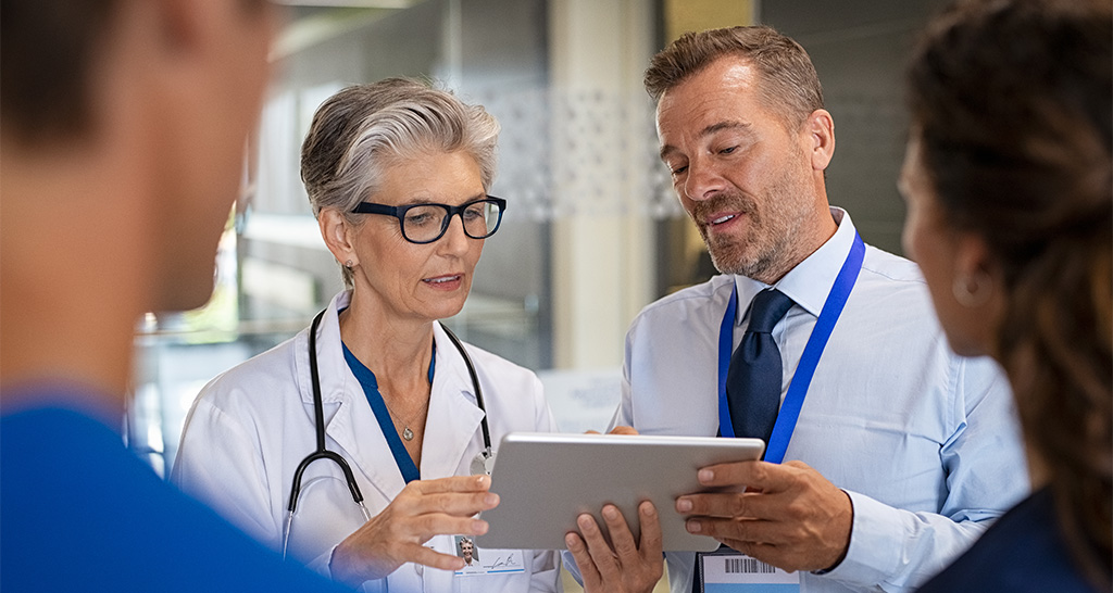 A man in business attire reviews information on a tablet with a doctor