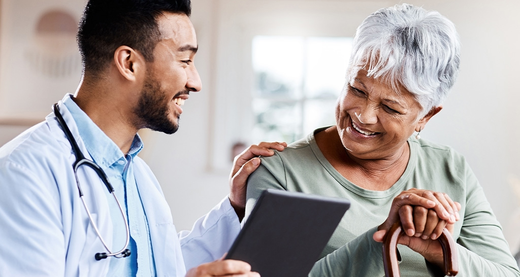 A doctor laughs with an elderly patient and rests his hand on her shoulder