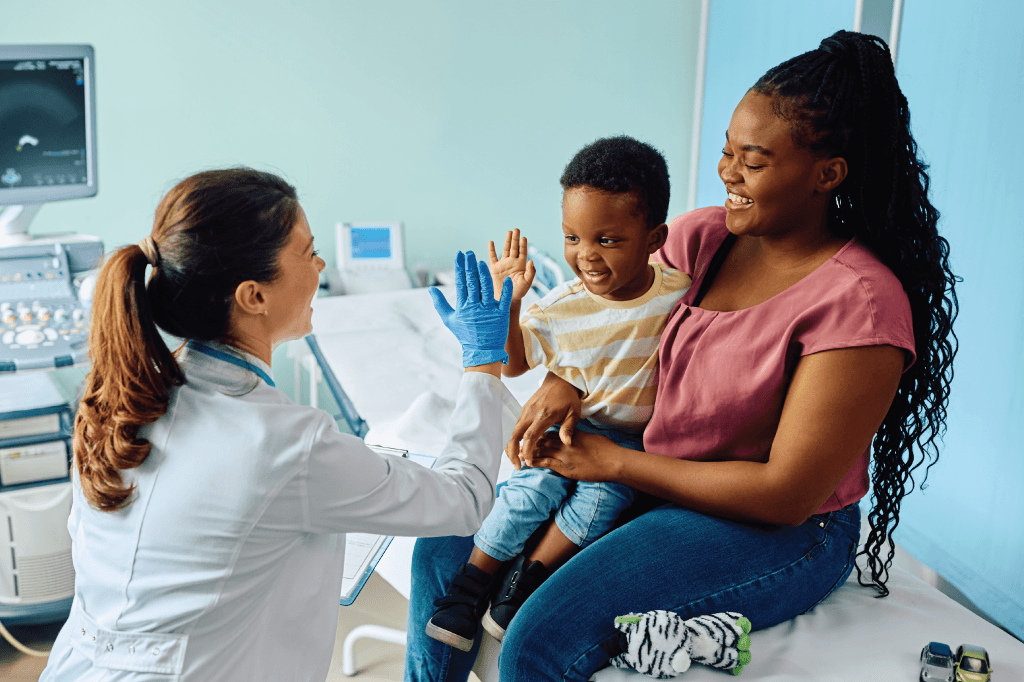 Female doctor and african american baby boy with her mother high-five physician in medical office.