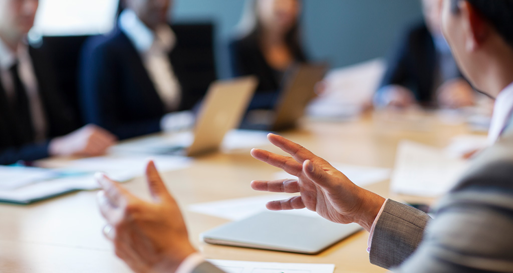 A man in professional wear speaks to a group around a conference table