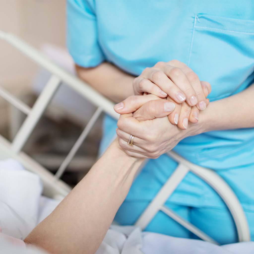 Female nurse holding senior woman's hand.