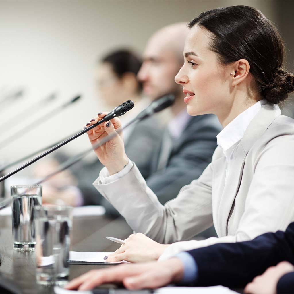 Talking to audience.  One member of the board speaking in microphone among other participants of meeting.