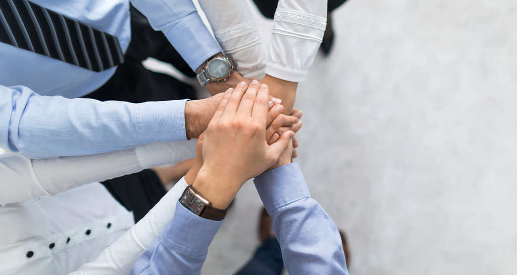 A group in professional attire puts their hands together in a circle