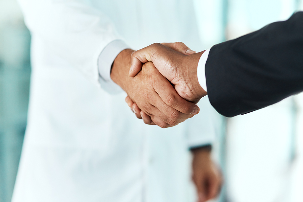 Close up of a doctor in a lab coat and a person in a suit shaking hands.