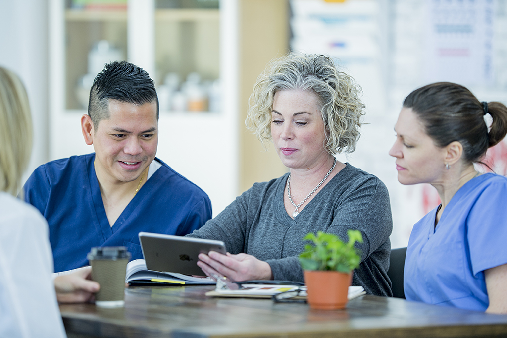 Three nurses look at a tablet.