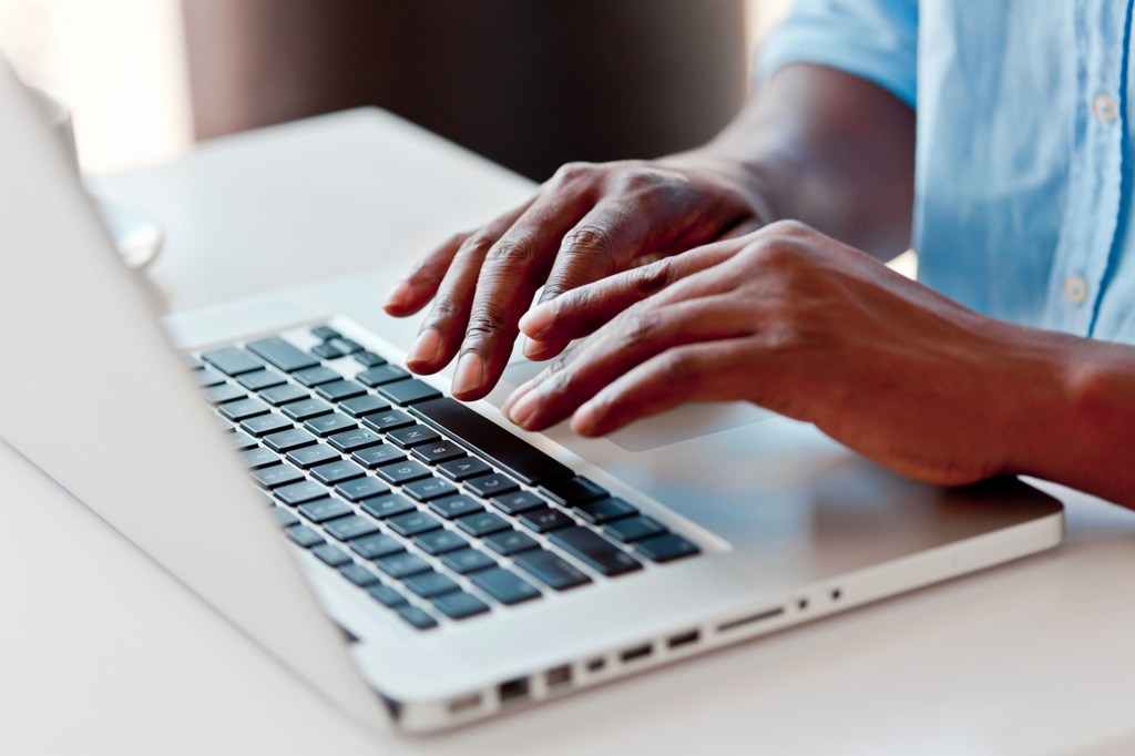 Individual in a blue button up shirt typing on a laptop. 