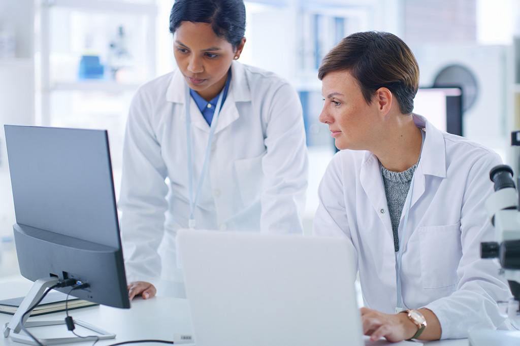 Two doctors in white lab coats look at a computer.