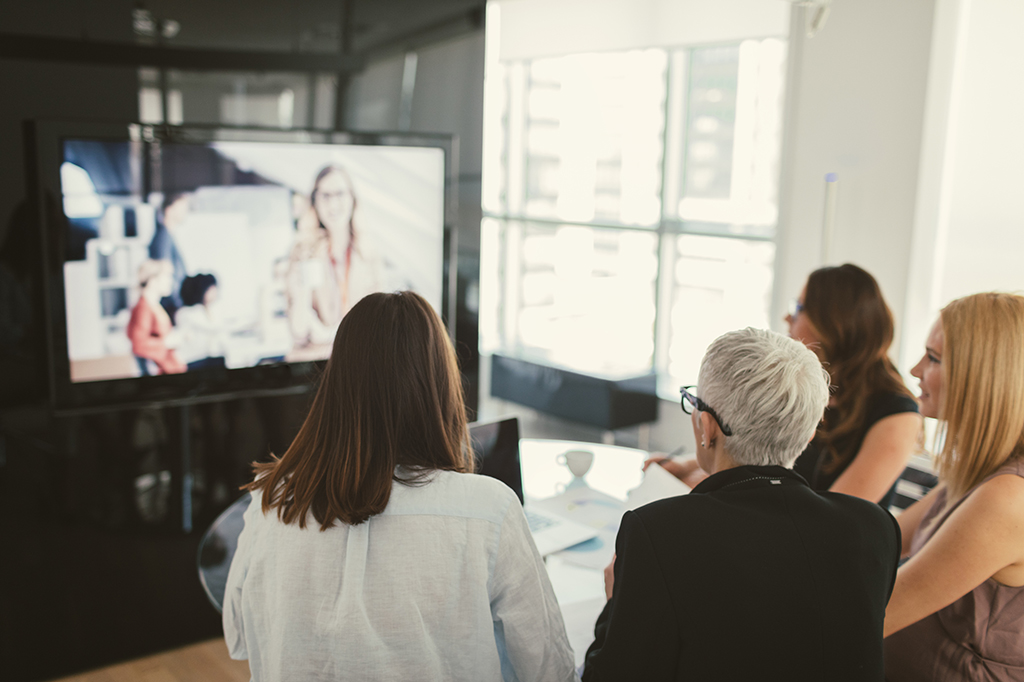 Four professionals watch a training video on a screen.