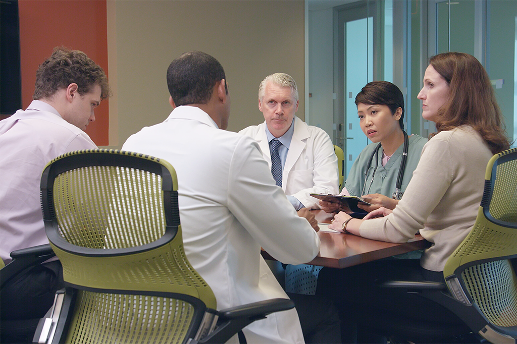 Five healthcare professionals sit at a table together.