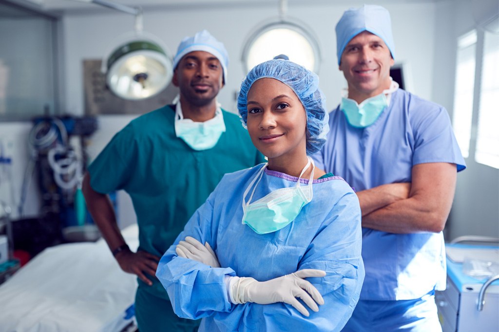 Three surgeons stand with crossed arms in an operating room.