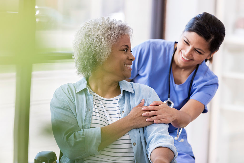 An elderly woman in a wheelchair is helped by a friendly nurse