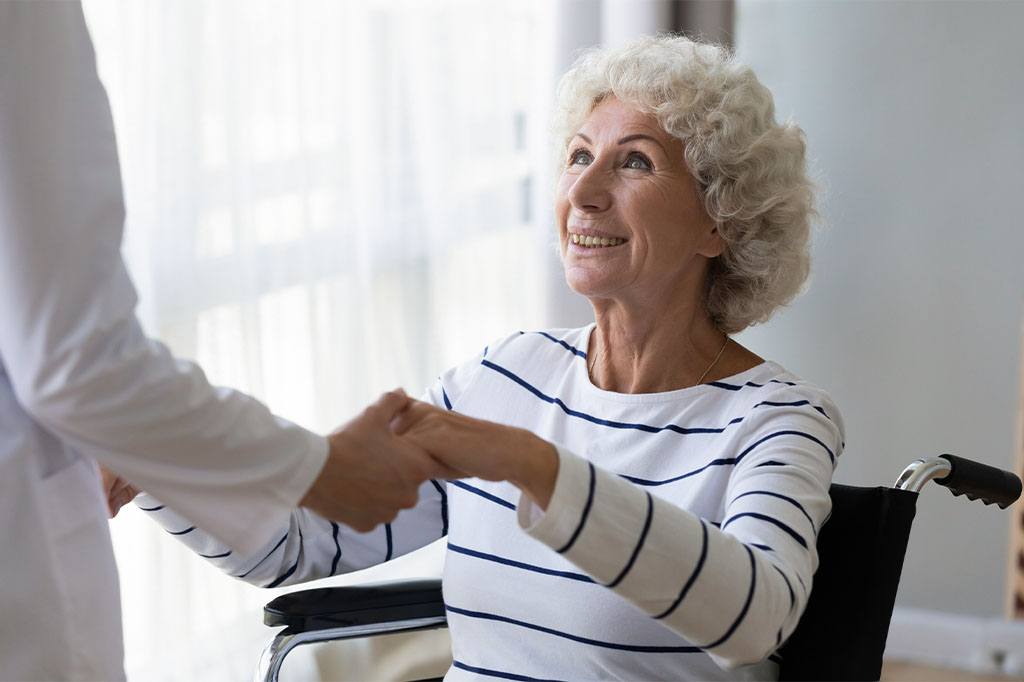 A doctor helps an elderly patient stand up out of her wheelchair