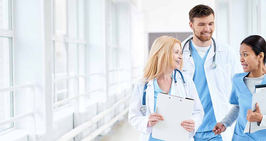 A trio of doctors have a conversation in a hospital hallway