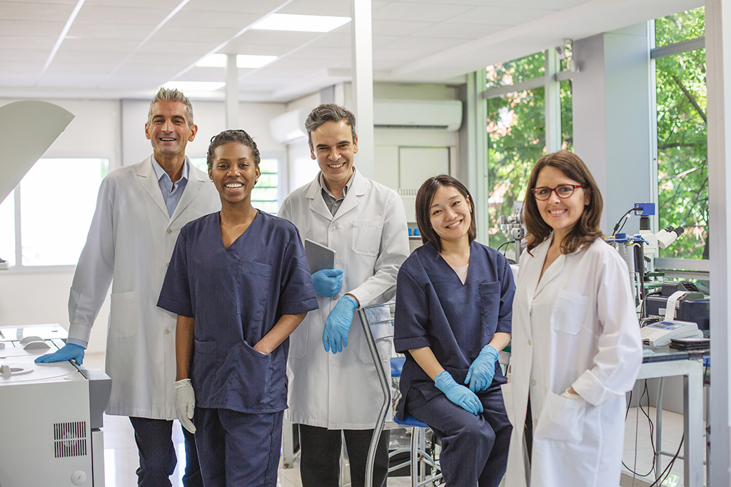 A group of doctors and nurses posing in a lab together smiling at the camera.