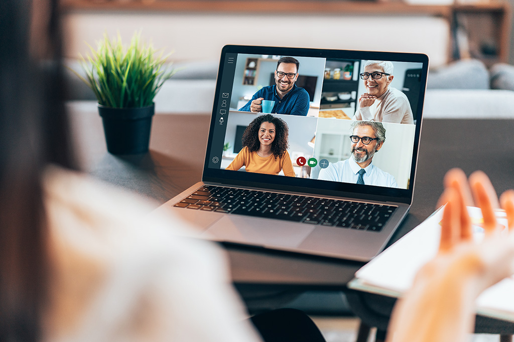 A woman uses a laptop to video call with four other people.