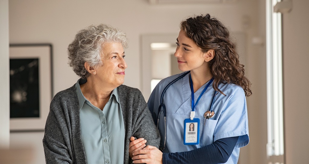 A nurse has her arm around an elderly patient and is helping her walk.