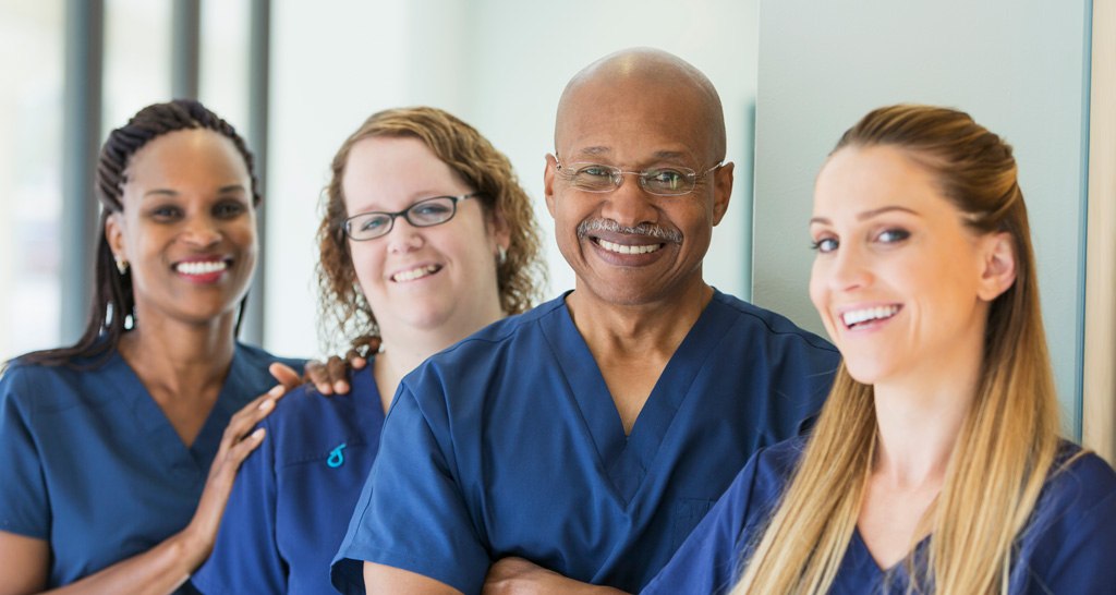 A group of four nurses smile at the camera.